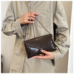 Detail of dark brown oil-wax leather envelope bag with golden chain strap on model
