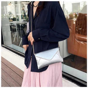 Detailed view of silver metallic envelope bag featuring natural texture and gold chain strap