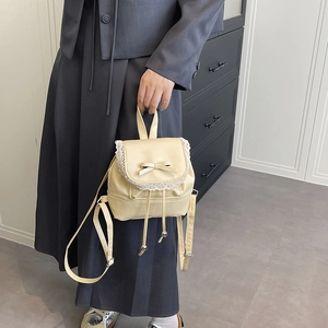 Chic cream leather backpack with lace trim and bow detail held in a home setting