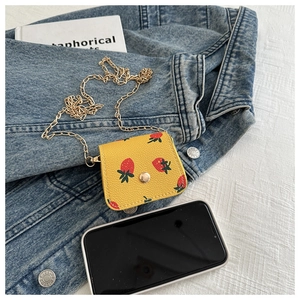 Détail du mini sac jaune aux fraises avec chaîne dorée à côté d'un smartphone