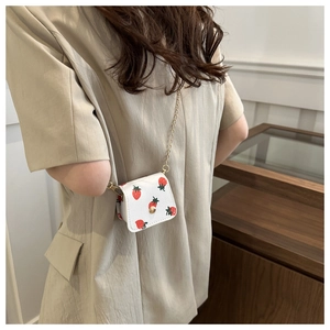 Détail d'un mini sac avec imprimé fraise et bandoulière chaîne dorée sur cuir blanc