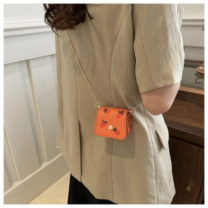 Detail view of mini strawberry print crossbody bag with gold chain strap worn by a model