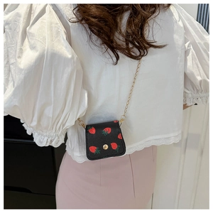 Détail du mini sac bandoulière à motif fraise avec chaîne dorée porté par le mannequin