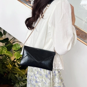 Chic black envelope shoulder bag with gold chain strap on model with floral skirt