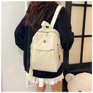 Detail view of the beige nylon backpack showing the front flap pocket and dual zipper design