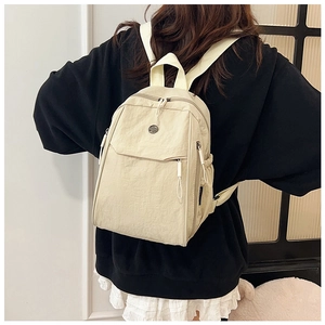 Back view of model wearing a beige nylon backpack with multiple zipper compartments