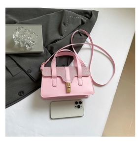 Detail of light pink crossbody bag with glitter flap and gold clasp next to a phone