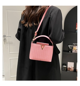 Pink woven handbag with golden V-shaped metal logo and textured crossbody strap