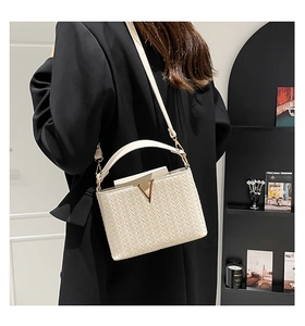 Détail du tissage chevrons beige et de la boucle dorée en V sur le petit sac carré élégant