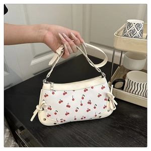 Detail of white underarm bag with red cherry prints and adjustable side bow accents