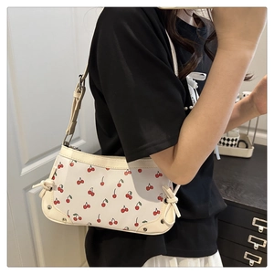 Detail of white underarm bag with red cherry print and beige leather trim on model