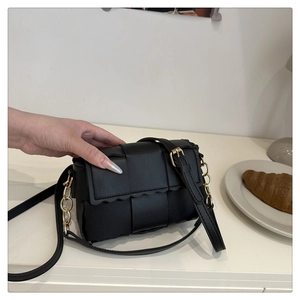 Détail de la texture en cuir tressé noir et des ferrures dorées du sac bandoulière chic