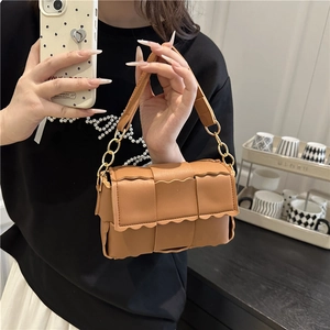Sac bandoulière tissé marron avec bords festonnés et chaîne dorée sur un mannequin
