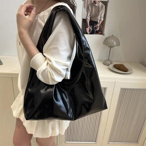 Minimalist black glossy large tote bag worn as a shoulder bag in a stylish home setting