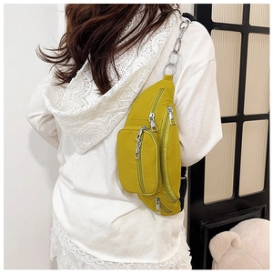 Detail of yellow nylon chest bag with silver metal zippers and chain strap on model