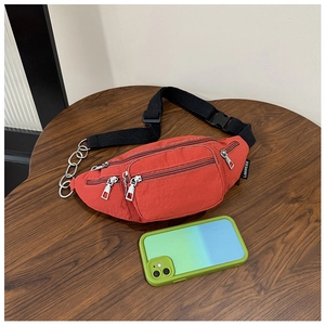 Detail of red nylon waist bag with metal chain accents and multi-zipper compartments