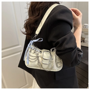 Detail of cream shoulder bag featuring metal chains, star charms and a blue checkered bow