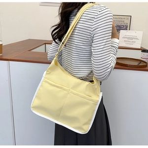 Détail d'un grand sac bandoulière jaune en toile avec bordure blanche porté par un mannequin
