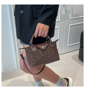 Detalle de un bolso bandolera de leopardo marrón con asas de cuero y correa desmontable