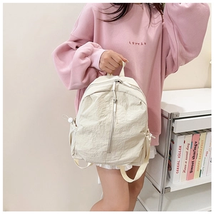 Detail of minimalist beige nylon backpack featuring side drawstring pockets and zippers