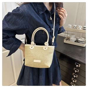 Detail of handwoven beige straw tote bag featuring round handles and leather patch