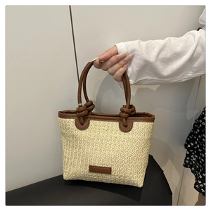 Detail of a straw bucket bag with brown leather handles and woven texture finish