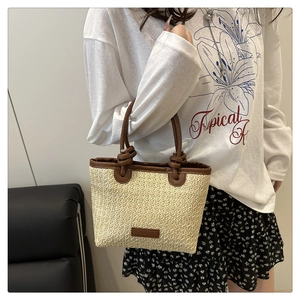 Detail of hand-woven straw bucket bag with brown leather handles and knot design