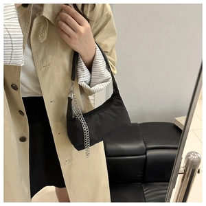 Detail of a black nylon underarm bag with silver chain strap worn with a trench coat