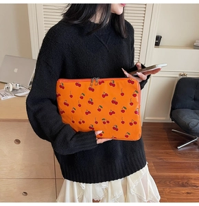 Chic orange cherry pattern laptop sleeve held by a model in a cozy indoor setting