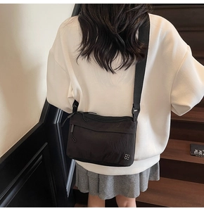 Rear view of a black nylon messenger bag with wide shoulder strap on a model