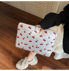 Detailed view of white cherry print laptop sleeve with dual zippers held by a hand