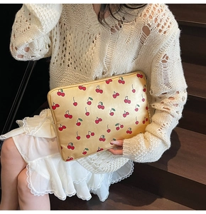 Close-up of champagne gold envelope clutch with red cherry print and zipper closure