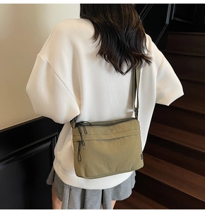 Back view of a green nylon messenger bag with multiple zippers and adjustable strap
