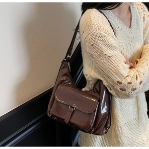Detail view of glossy dark brown patent leather shoulder bag with a large buckled front pocket