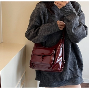 Chic burgundy patent leather hobo bag with front pocket and buckle on a model