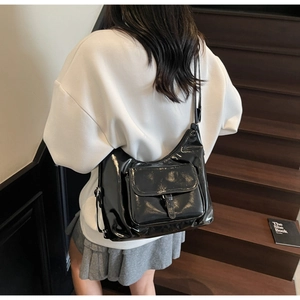 Detail of minimalist black patent leather crossbody bag with front flap pocket and strap