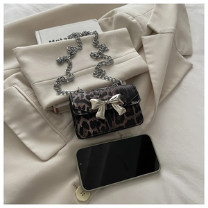 Detail of mini leopard print bag with silver bow buckle and chain on beige fabric