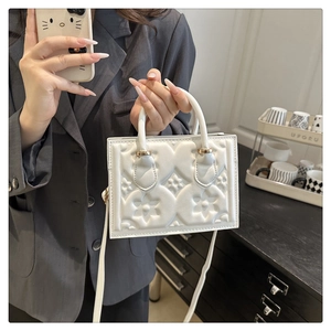 Detailed macro view of white embossed leather handbag with golden metal hardware