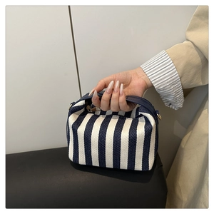 Detail of blue and white striped woven tote with navy leather handle and gold hardware