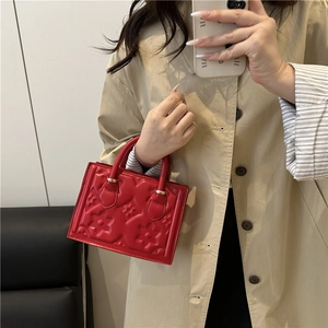 Elegant red embossed handbag with dual handles and floral patterns in a mirror selfie view