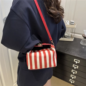 Red and white striped canvas crossbody bag worn by a model in a minimalist indoor setting