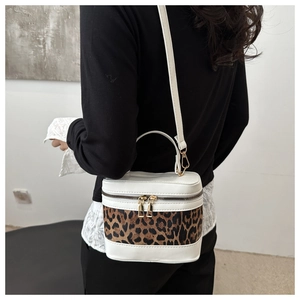 Detail view of a white box-shaped crossbody bag with bold leopard print and dual zippers