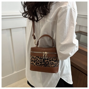 Detailed view of leopard print bucket bag with brown leather trim and golden zippers