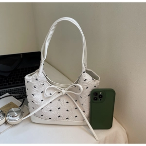Détail du sac crème à nœud papillon avec texture florale et ornement de ruban blanc