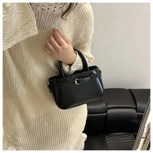 Detalle de un mini bolso negro brillante con hebilla metálica y una silueta redondeada