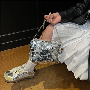 Silver sequin shoulder bag with gold metal chain strap worn by model in a stylish setting