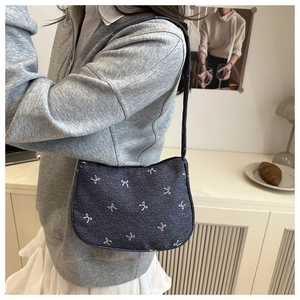 Detail of a dark denim underarm bag featuring colorful bow patterns and slender shoulder strap