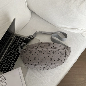 Grey corduroy crossbody bag with black heart prints on a minimalist sofa background