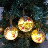 Three glowing Christmas ornaments with LED lights, greenery and red berries on tree