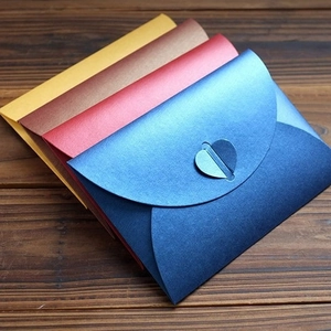 Pearlescent heart clasp envelopes in gold, bronze, red, and blue on dark wood background